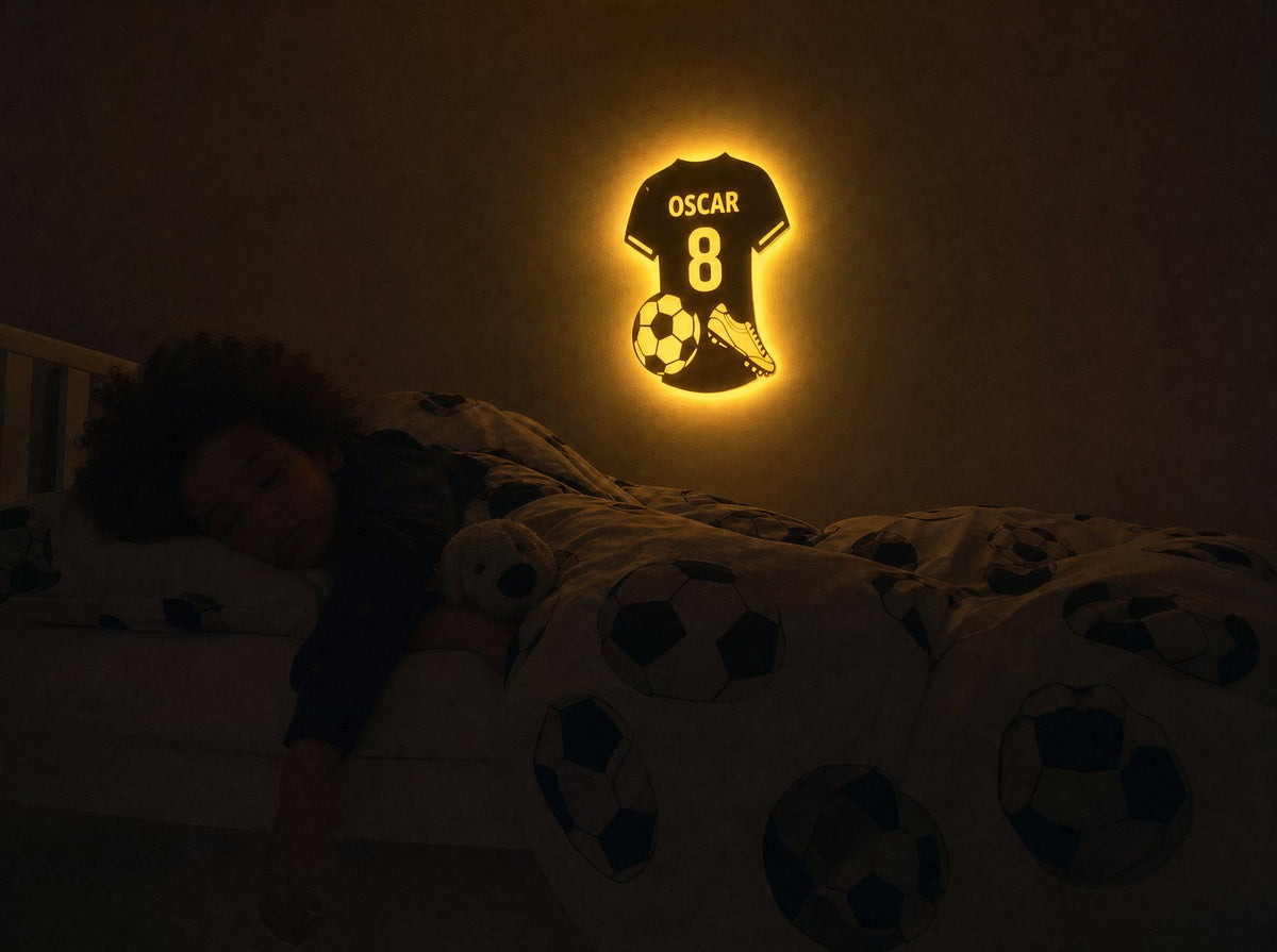 A boy asleep while his name glows softly on the wall above the bed