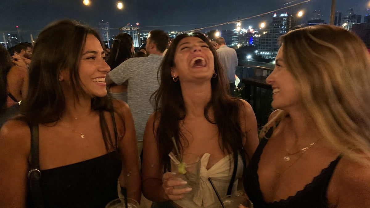 Three friends laughing at a rooftop bar