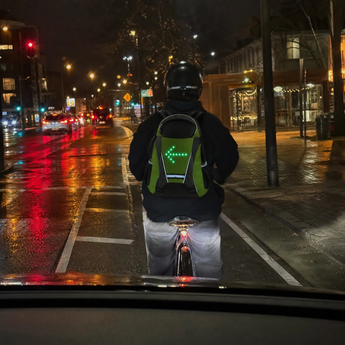 A driver's view at night of a cyclist whose Beacon backpack shows a left arrow