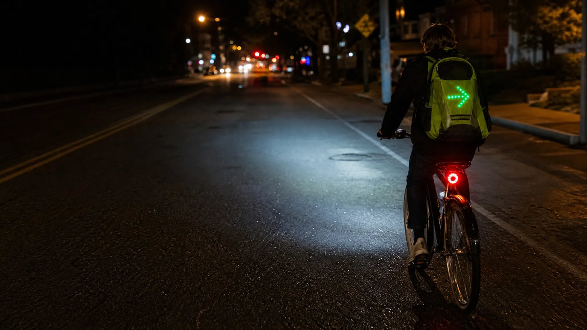 A cyclist at night with a Beacon right arrow, a headlight beam on the road and a red brake light