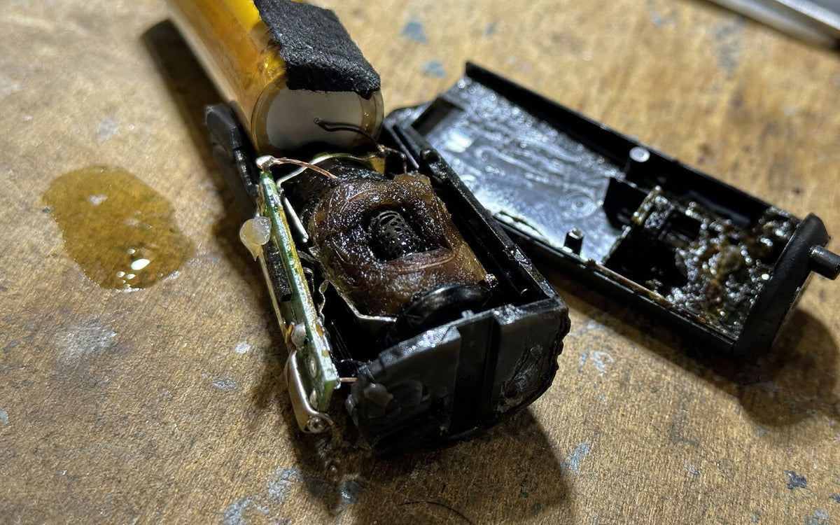 A disposable vape pried open, showing the battery, wires and a burnt coil