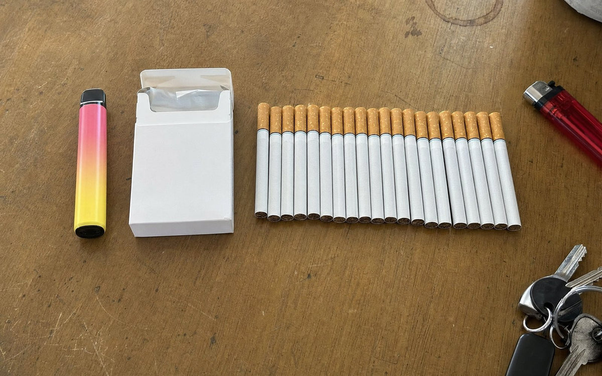 One disposable vape next to a pack of 20 cigarettes laid out in a row