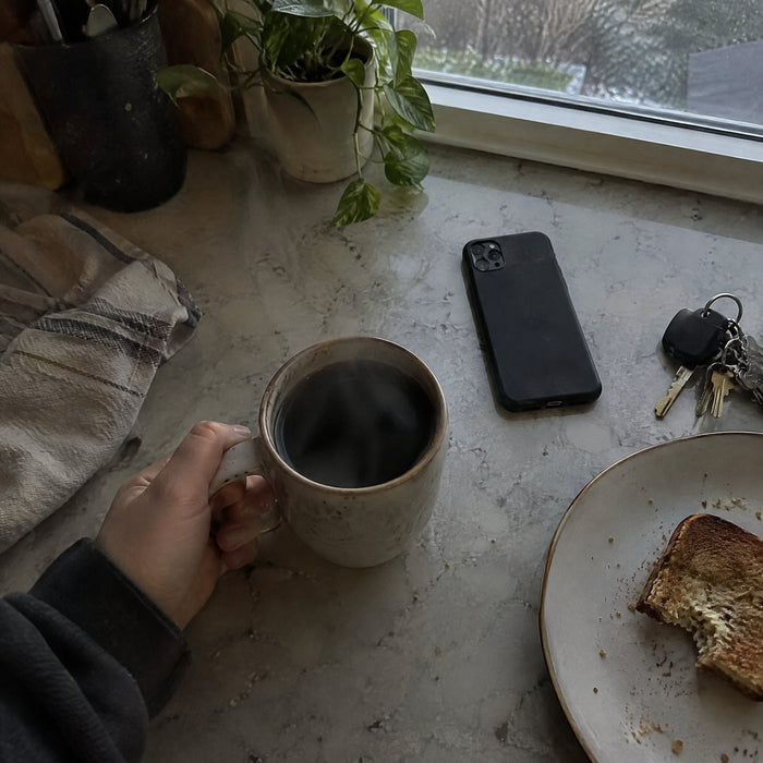 Hand holding a coffee mug next to a phone and keys