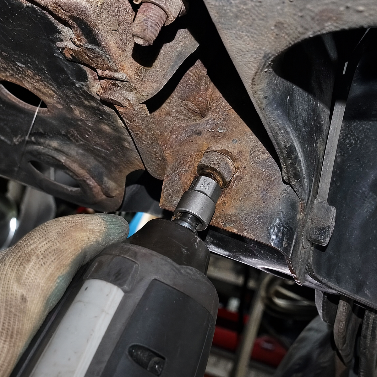 Extractor socket on an impact wrench removing a rusted rounded bolt under a truck