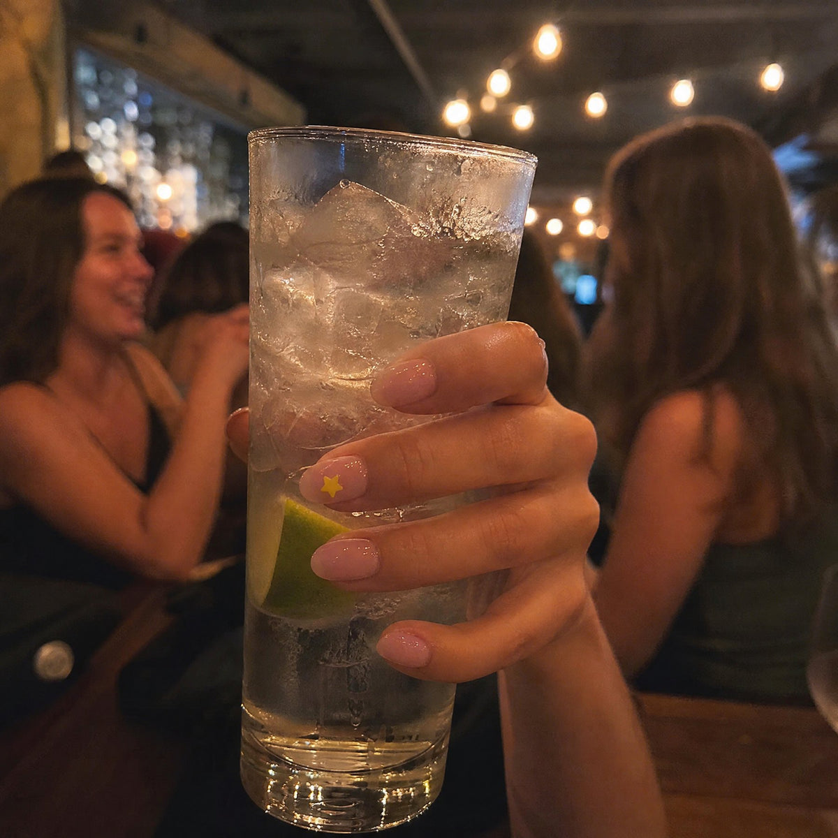 Clear NightCheck sticker on a nail while holding a drink at a bar