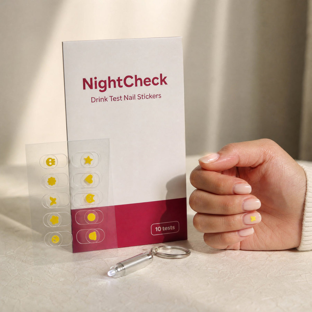 NightCheck drink test nail stickers package with sticker sheet, a hand wearing one sticker and a pocket light