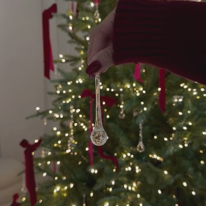 Clear glass crystal drops being hung on a lit Christmas tree with red velvet bows