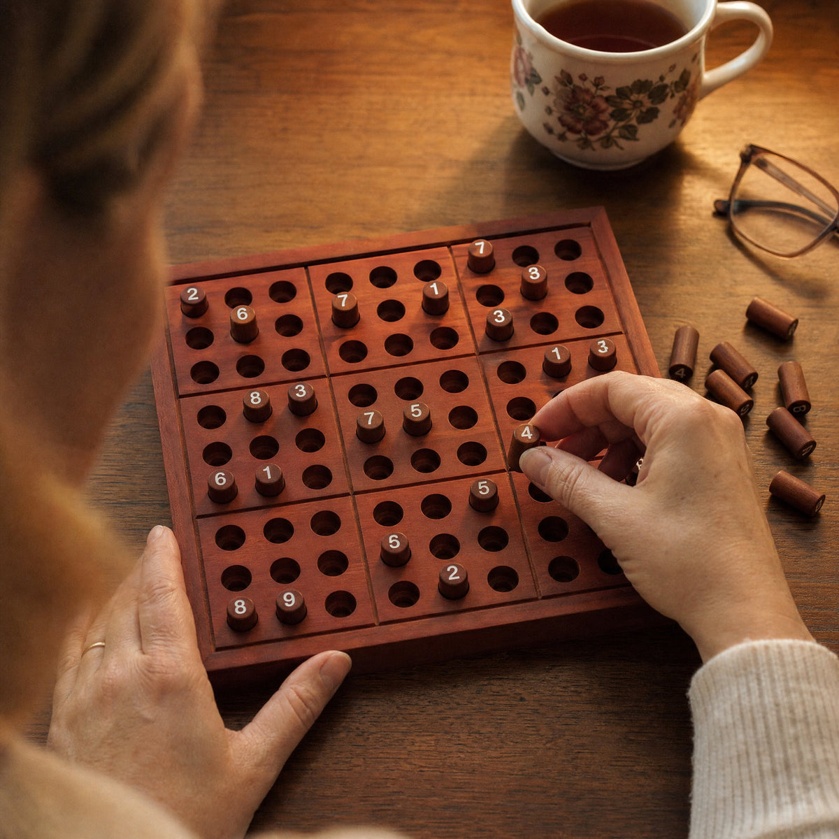 Hands placing a numbered wooden peg on the sudoku board