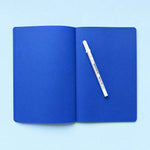 Open blank cobalt blue notebook with white gel pen